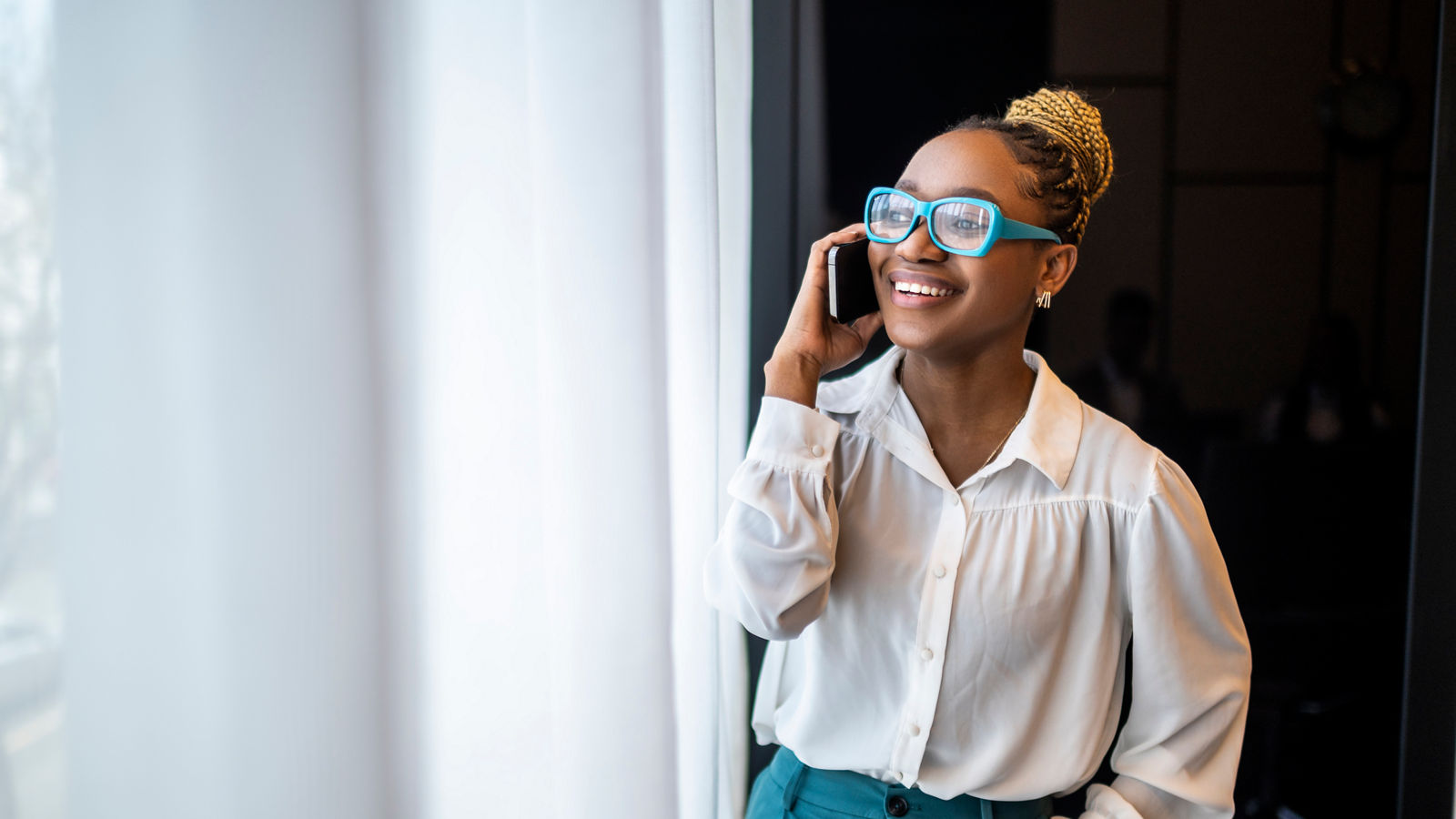 A woman with blue eyeglasses and a bun standing by the window