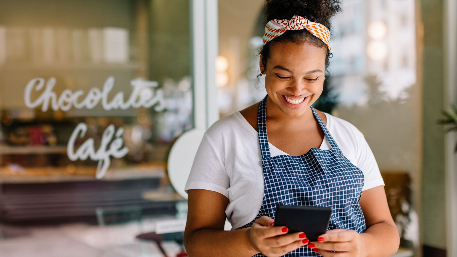 Entrepreneur standing in a coffee shop, using a digital tablet for easy cafe management. Successful small business owner reading her online reviews, staying connected to her customers