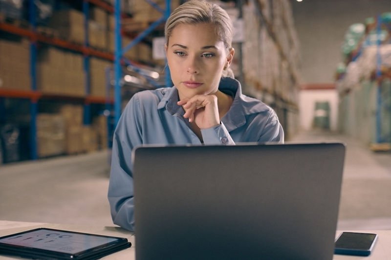 Woman thinking in warehouse looking at laptop for logistics