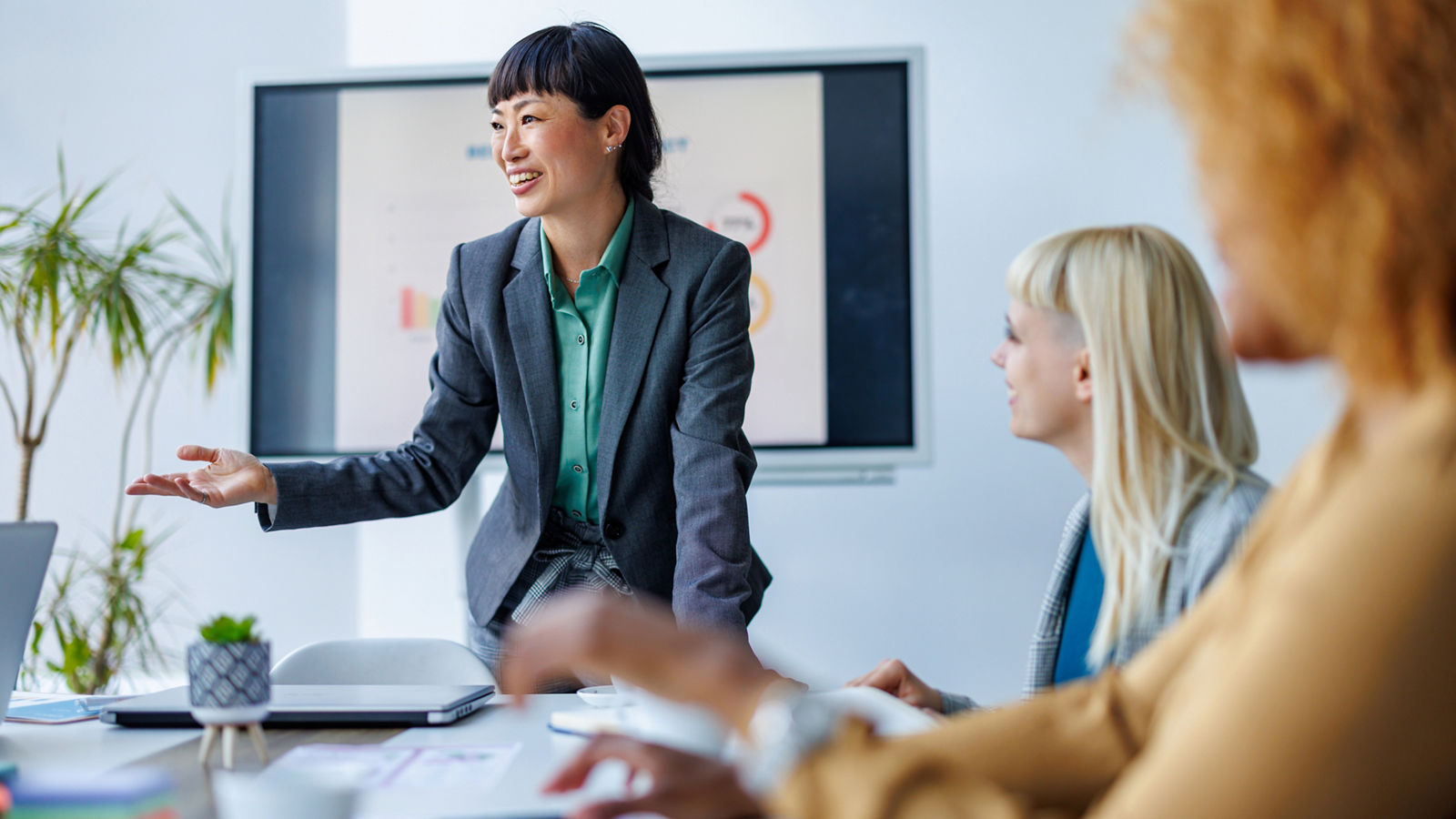 A person leading a business meeting with colleagues in a bright office setting, presenting data on a screen