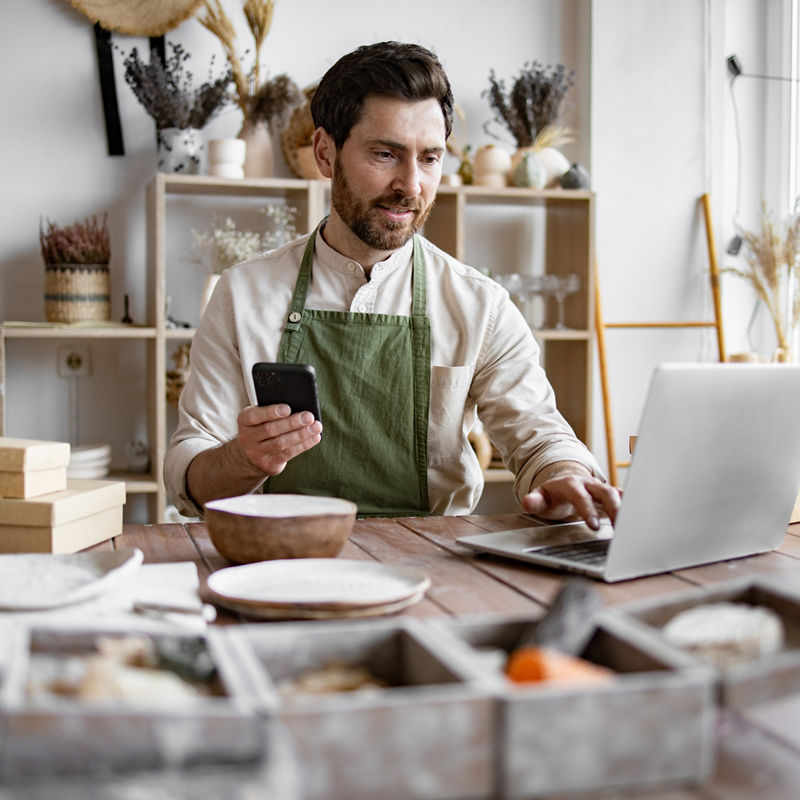 Successful guy store employee with ceramic tableware shoots photos on smartphone. Charismatic Caucasian man seller in souvenir shop takes pictures of goods at phone for posting on social networks.