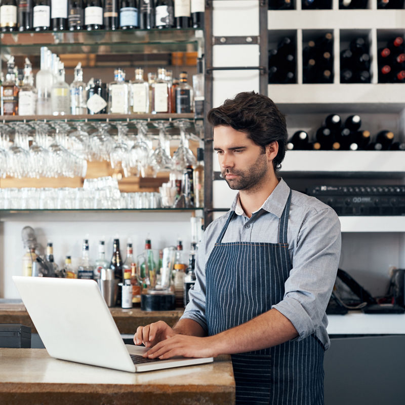 Cropped shot of a handsome young man working on a laptop while standing in his coffee shop