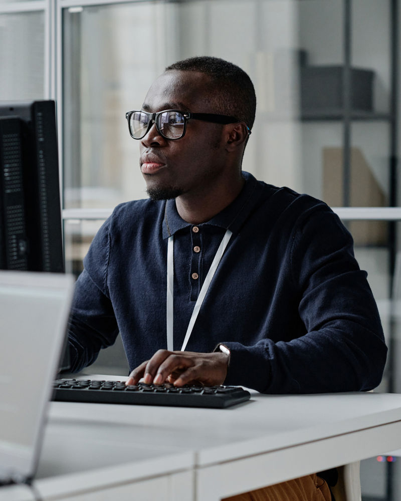Developer in eyeglasses concentrating on his online work on computer sitting at workplace