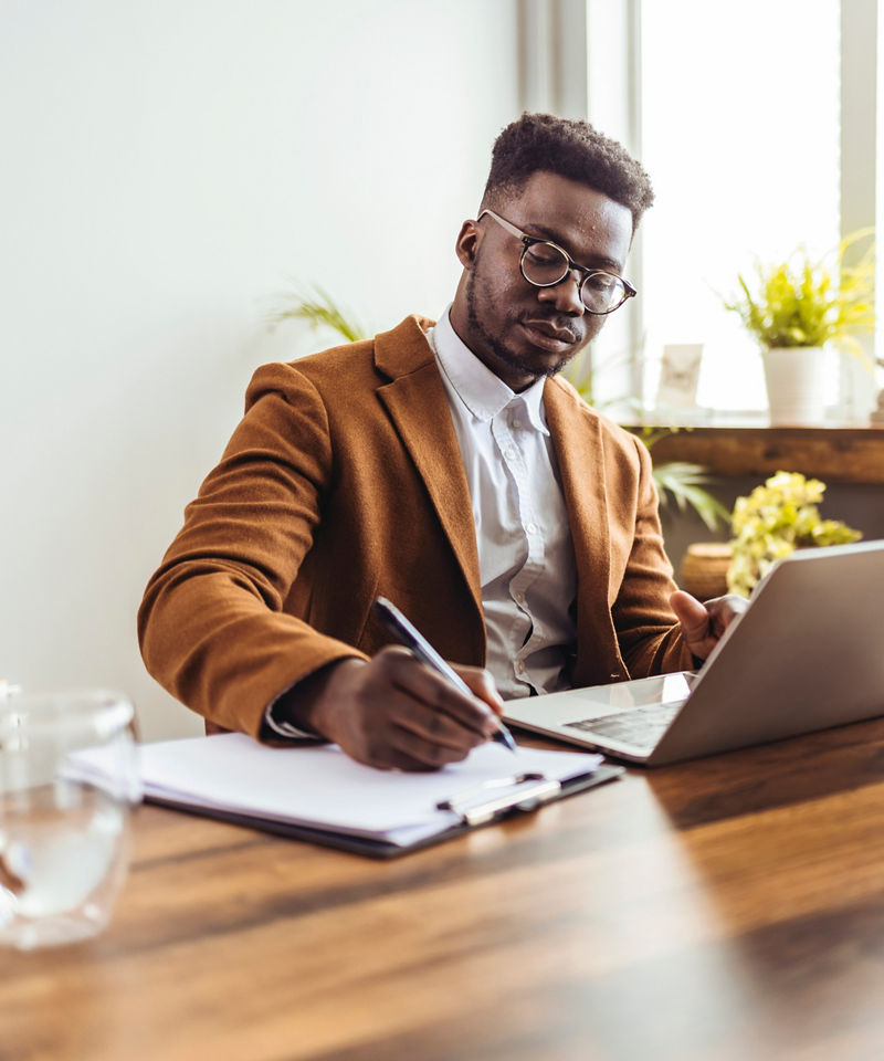 Focused businessman writing at desk and referencing laptop