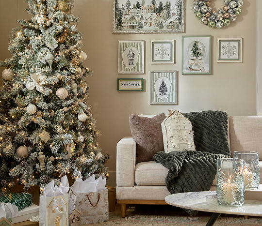 A neutral toned living room is decorated for Christmas with a frosted tree, a cream couch decorated with throw pillows and a blanket, and other cute winter decor items from pOpshelf.