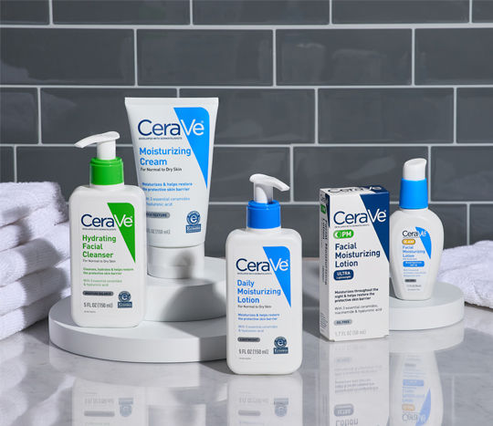 A neutral grey and white bathroom features an array of CeraVe products from pOpshelf displayed between folded towels on a white sink top.