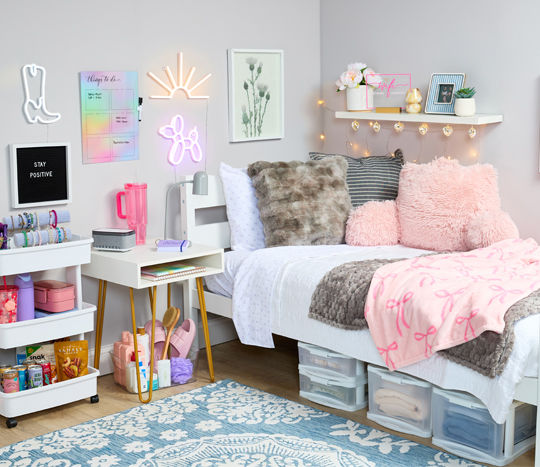 Decorated dorm with pink throw, pink study pillow, underbed plastic storage, fun lights and decor, with bath supplies, water bottles, snacks & more.