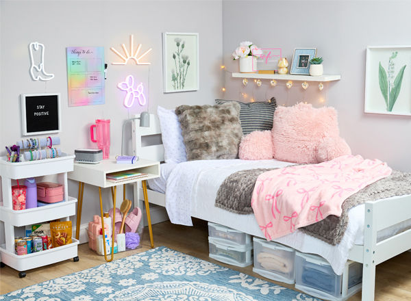 Decorated dorm with pink throw, pink study pillow, underbed plastic storage, fun lights and decor, with bath supplies, water bottles, snacks & more.