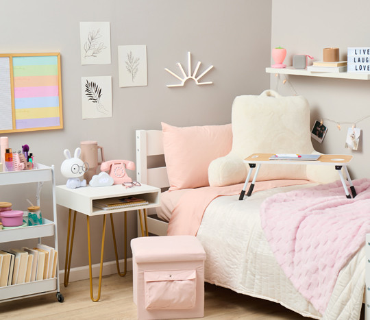 Dorm room decorated with pastel ans neautral tones:pink storage ottoman, pink throw, white study pillow, lap desk, white storage cart, vintage pink phone and more.