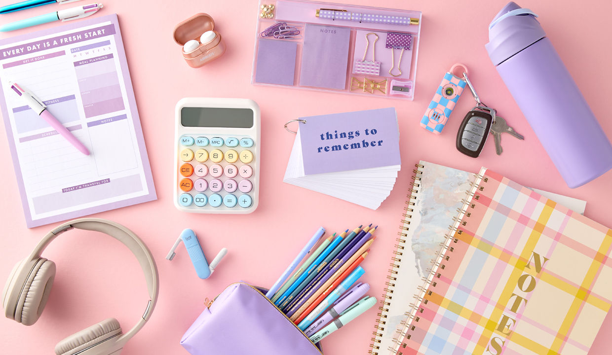 Pastel back-to-school supplies: spiral notebooks, purple pouch with colored pens & pencils, calculator, water bottle, earbuds & more.
