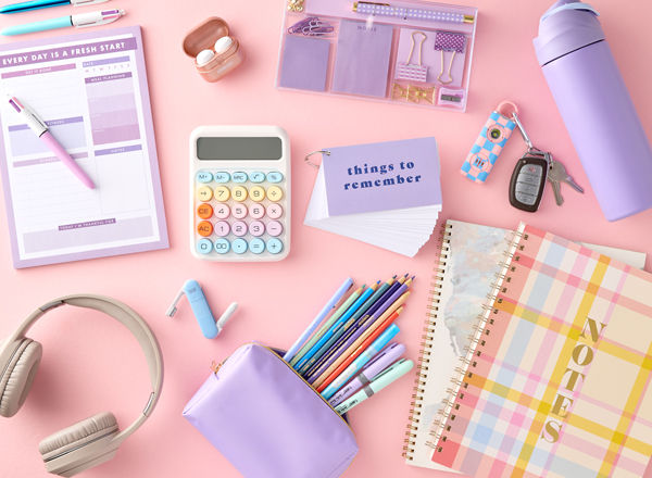 Pastel back-to-school supplies: spiral notebooks, purple pouch with colored pens & pencils, calculator, water bottle, earbuds & more.