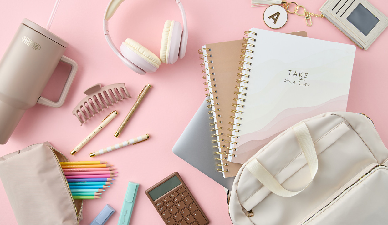 Neutral-toned back-to-school supplies: cream backpack, white headphones, spiral notebooks, tan pouch with colored pencils pastel highlighters, pens & more.