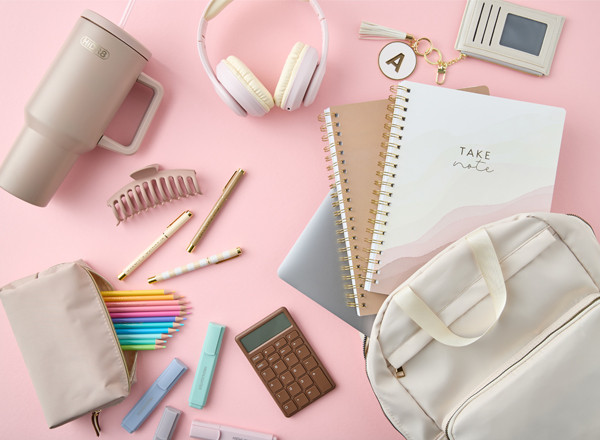 Neutral-toned back-to-school supplies: cream backpack, white headphones, spiral notebooks, tan pouch with colored pencils pastel highlighters, pens & more.