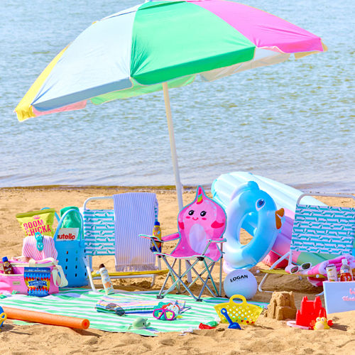 Beach scene with folding beach chairs, beach umbrella, beach towels, insulated coolers & sand toys.