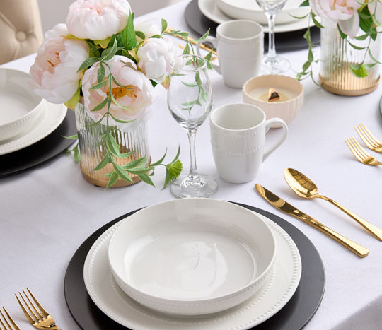 Elegant table set with white beaded dinnerware, black chargers, and gold flatware.