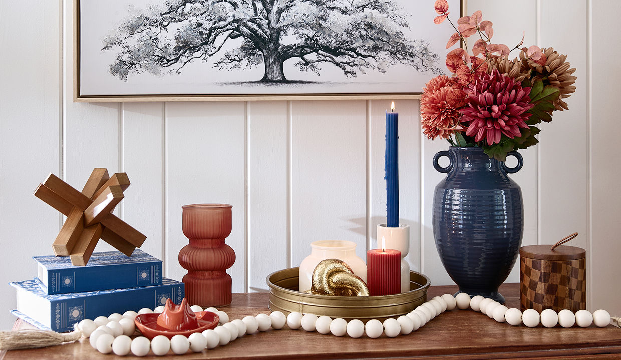 A wooden entryway table is decorated with orange, terracotta, cream, brass, and dark blue western-inspired decor including a mini cowboy hat, candles, vases, and decorative accents.
