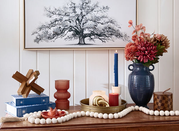 A wooden entryway table is decorated with orange, terracotta, cream, brass, and dark blue western-inspired decor including a mini cowboy hat, candles, vases, and decorative accents.