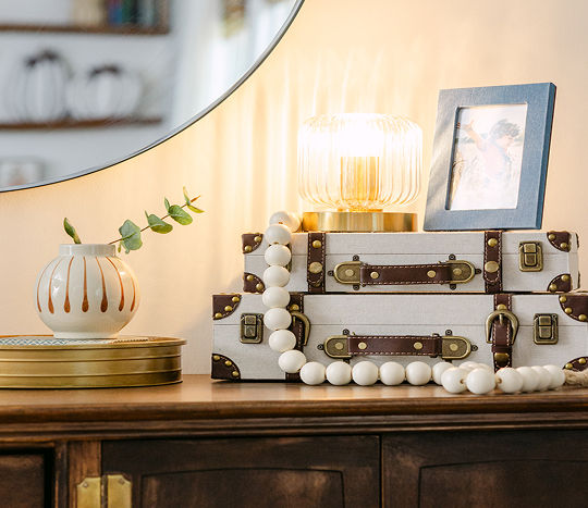 A wooden entryway table is decorated with orange, terracotta, cream, brass, and dark blue western-inspired decor including candles, vases, and decorative accents.