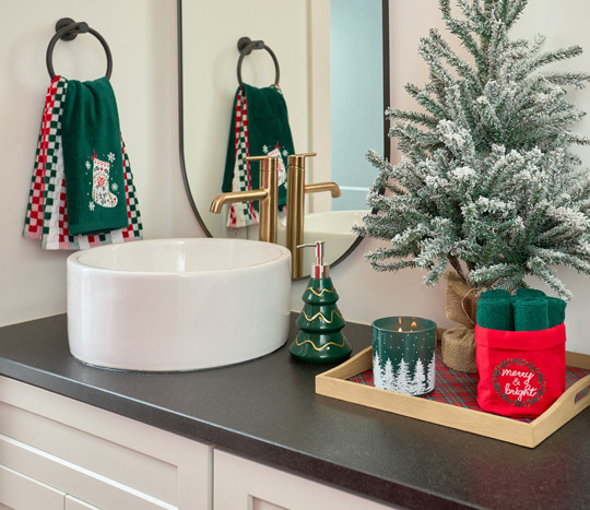 Bathroom decorated for Christmas with ferstive shower curtain, hand towels, bath rug, tree and gingerbread house soap pumps, and Christmas decor.