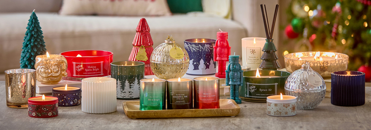 Christmas candles in various sizes, designs, and scents on a table in front of a Christmas tree.