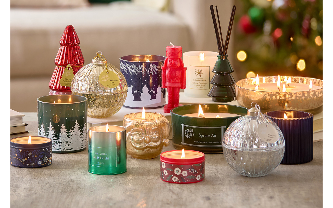 Christmas candles in various sizes, designs, and scents on a table in front of a Christmas tree.