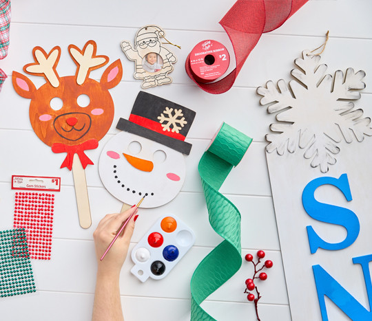 Christmas craft supplies: wooden handheld DIY masks, DIY snowflake porch leaner, green, red, and plaid wired ribbon, DIY plastic fillable ornaments & more.