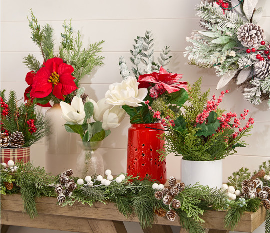 Five vases filled with faux Christmas florals and greenery and a flocked wreath: red & white poinsettias, frosted & flocked pine and pinecones, holly and berries, and more.