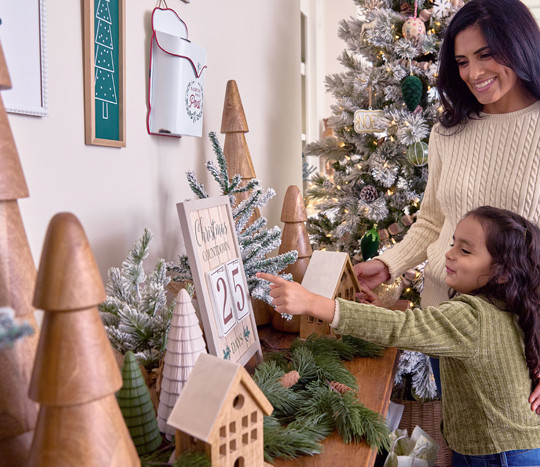 Mother & daughter decorating for Christmas with large wooden trees and winter wonderland decor.