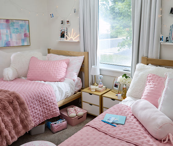 Decorated dorm with pink throw, white study pillow, underbed plastic storage, fun lights and decor, with bath supplies, water bottles, snacks & more.