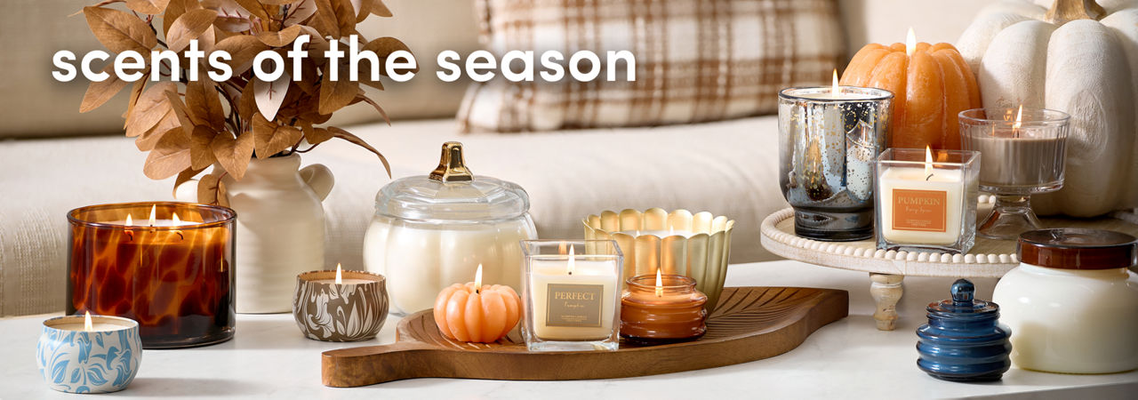 Couch with pillows and coffee table filled with various shaped and sized fall candles and vase with floral arrangement.