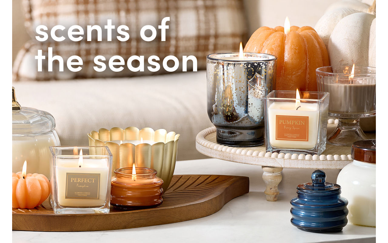 Couch with pillows and coffee table filled with various shaped and sized fall candles and vase with floral arrangement.