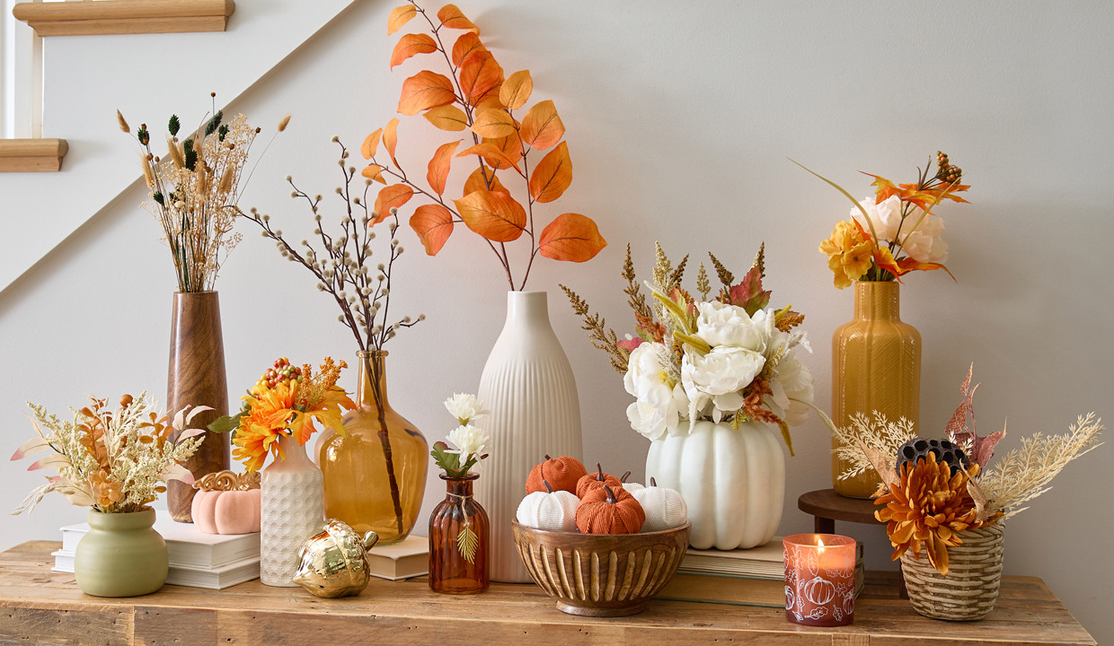 Fall floral bushes, branches, and picks in vases and premade fall floral arrangements on an entryway table.