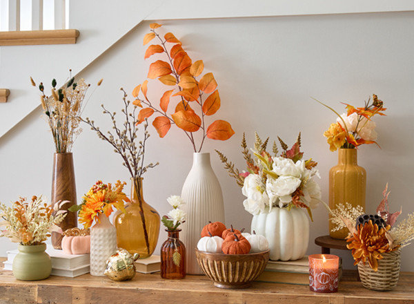 Fall floral bushes, branches, and picks in vases and premade fall floral arrangements on an entryway table.