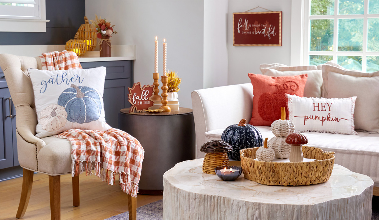 Den decorated for fall with blue pumpkin pillow, throw, wicker and metal pumpkin decor, fall wooden candleholders, and fall floral.