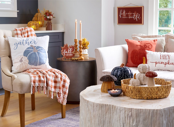 Den decorated for fall with blue pumpkin pillow, throw, wicker and metal pumpkin decor, fall wooden candleholders, and fall floral.