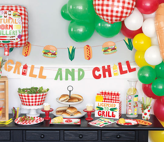 An outdoor table is decorated with “grill and chill” themed tablescaping decor including colorful accents and red gingham print.