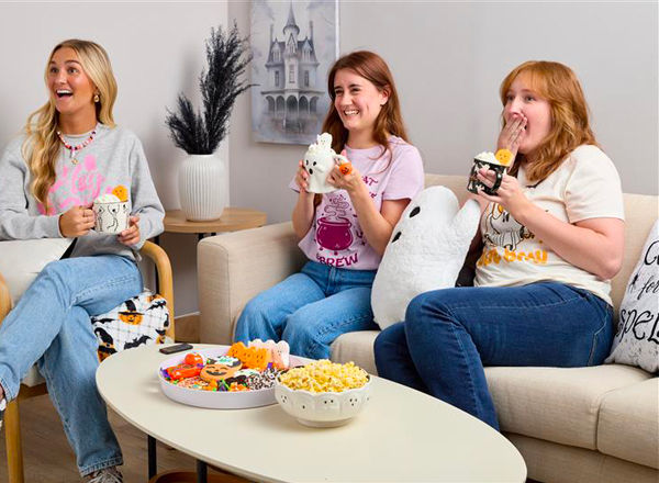 Girfriends in Halloween sweatshirts and t-shirts enjoying a candy charcuterie board, hot chocolate in cute Halloween mugs, and a scary movie.