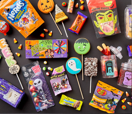 Various colorful halloween candy on a black background: Jelly Belly, marshmallow Peeps and pops, gummy zombie fingers and bat wings, decorated cookie pops, Reese's Pumpkins, Haribo Cears, candy corn, Krispy treats & more.