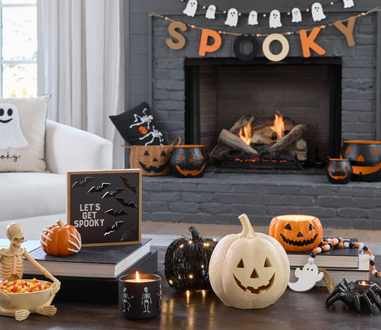 Coffee table with pumpkin sign, black LED candles, pumpkins, and candle in front of sofa with 'BOO' pillow