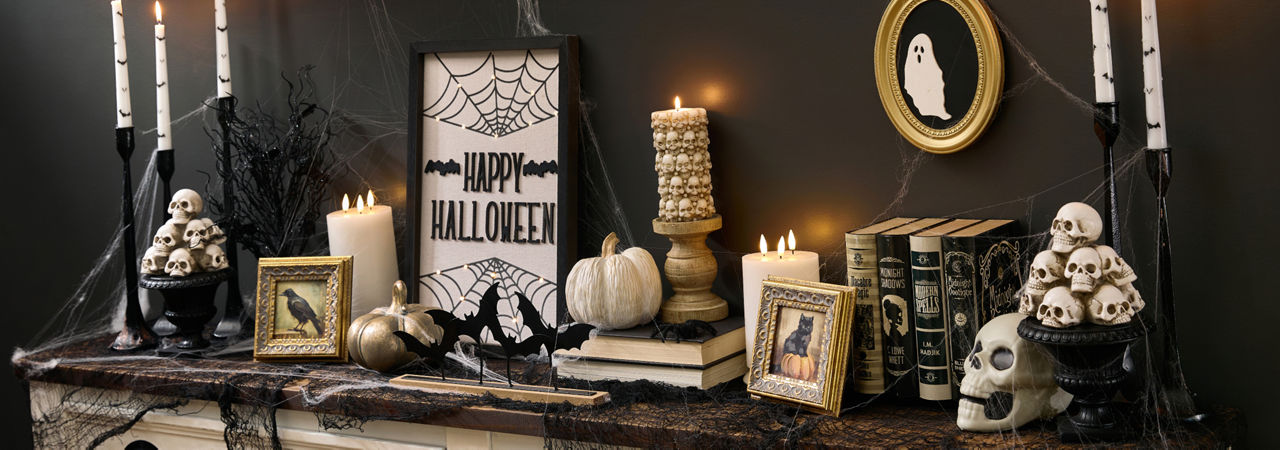 A spooky Halloween-themed foyer table is decorated with classic Halloween decor from pOpshelf like skeletons, framed art, bat candlesticks, a spider web tablecloth, brass pumpkins, and more affordable spooky finds.