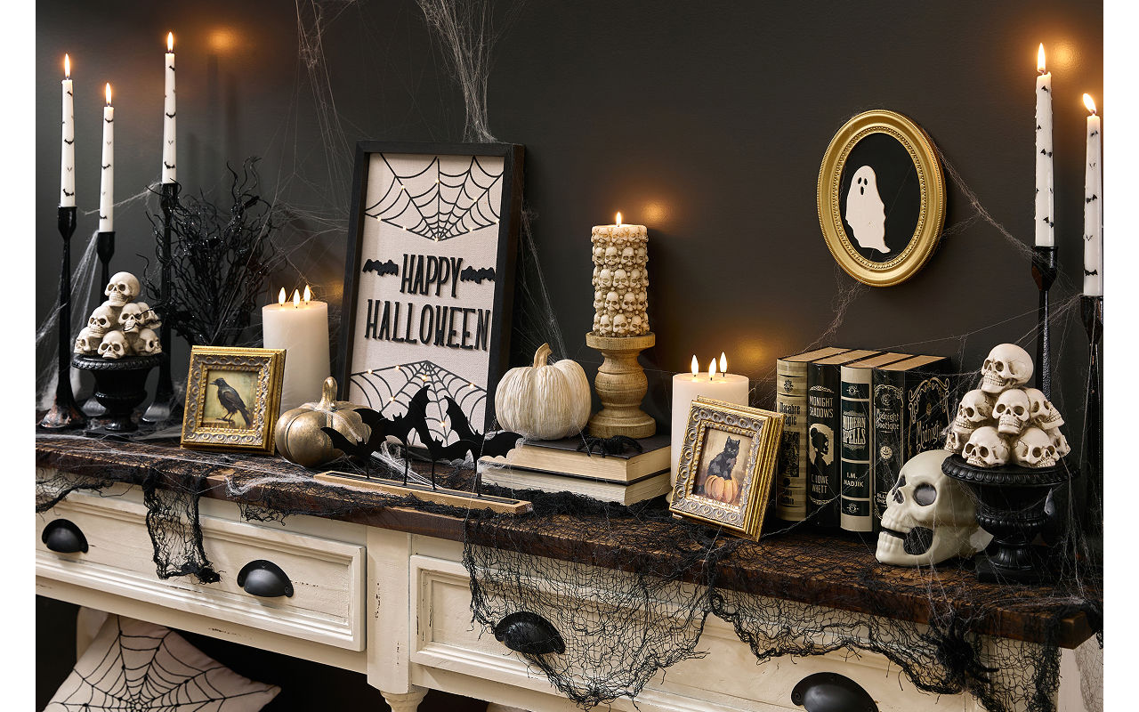 A spooky Halloween-themed foyer table is decorated with classic Halloween decor from pOpshelf like skeletons, framed art, bat candlesticks, a spider web tablecloth, brass pumpkins, and more affordable spooky finds.