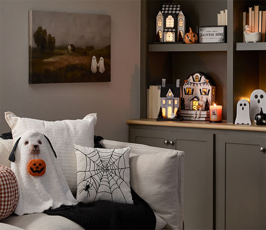 A neutral toned living room  decorated with classic Halloween decor from pOpshelf including ghosts, a spooky cozy blanket, plush pumpkin pillows, viral haunted houses with lights, moody Halloween framed wall art, and seasonal fall candles.
