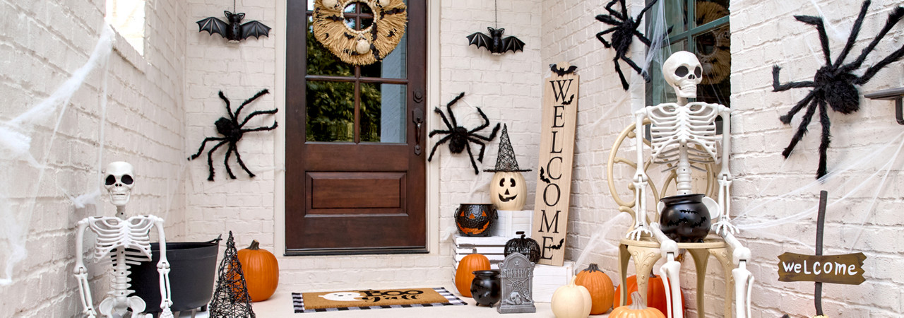 Front porch decorated for Halloween with giant spiders, skeletons, pumpkins and jack-o-lanterns, solar bat lanterns, witches hats, and a Welcome porch leaner.