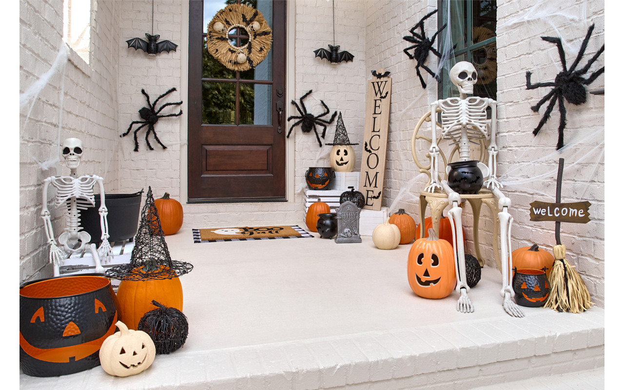 Front porch decorated for Halloween with giant spiders, skeletons, pumpkins and jack-o-lanterns, solar bat lanterns, witches hats, and a Welcome porch leaner.