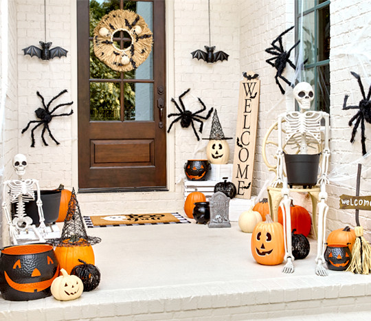 Front porch decorated for Halloween with giant spiders, skeletons, pumpkins and jack-o-lanterns, solar bat lanterns, witches hats, and a Welcome porch leaner.