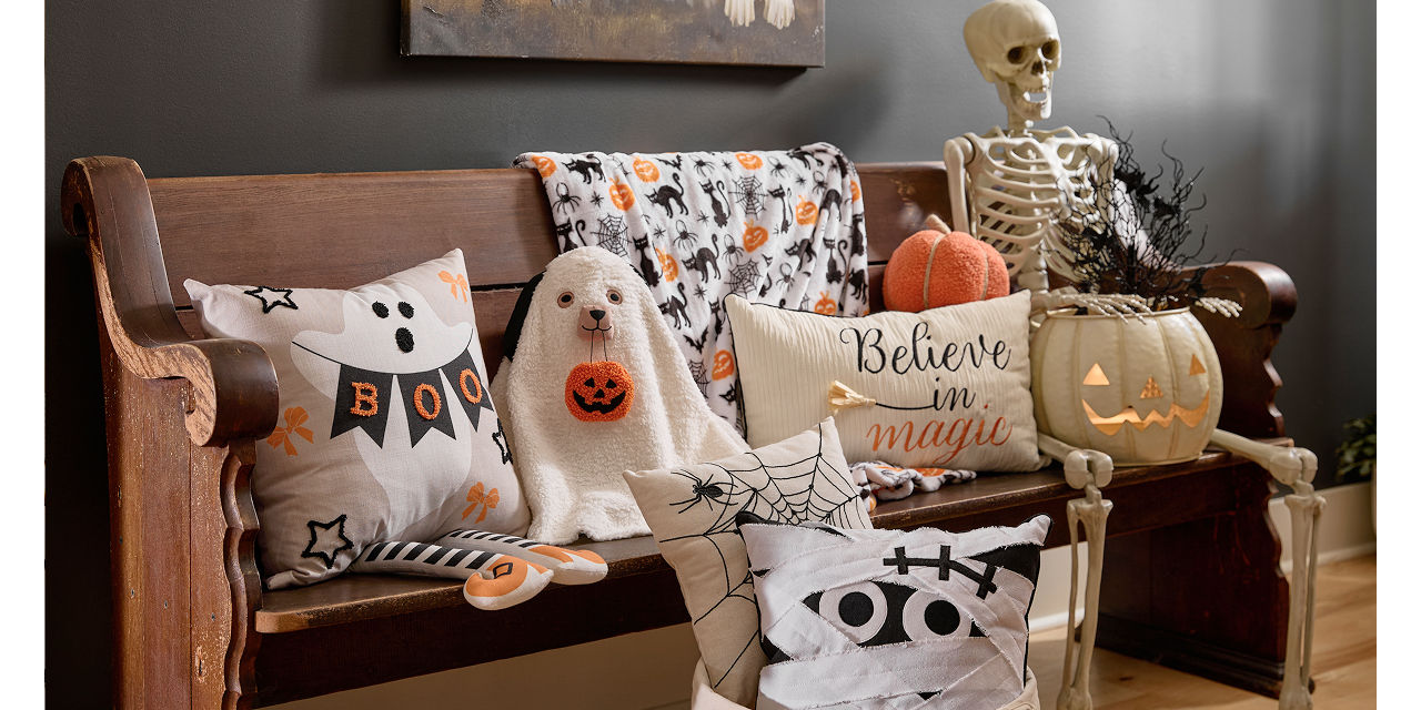 Halloween pillows lined up on a bench in a foyer: dog ghost pillows, mummy pillow, spiderweb pillow, and more.