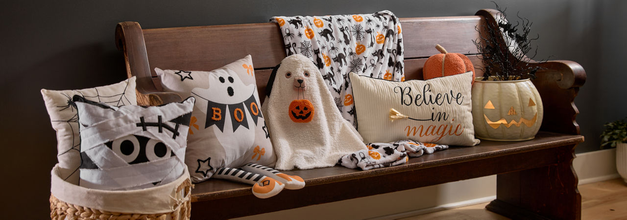 Halloween pillows lined up on a bench in a foyer: dog ghost pillows, mummy pillow, spiderweb pillow, and more.