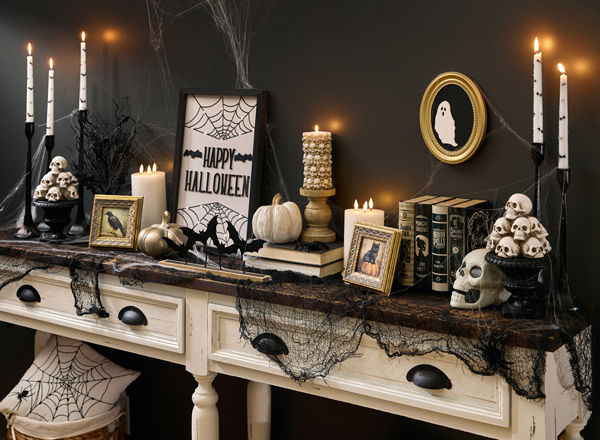 A spooky Halloween-themed foyer table is decorated with classic Halloween decorations from pOpshelf featuring skeletons, Halloween skulls, moody gothic-inspired framed art, bat candlesticks, a spider web tablecloth, golden pumpkins, and more affordable Halloween themed finds.