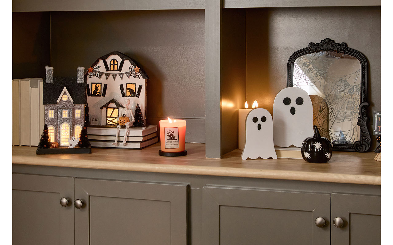 A neutral toned living room  decorated with classic Halloween decor from pOpshelf including ghosts, a spooky cozy blanket, plush pumpkin pillows, viral haunted houses with lights, moody Halloween framed wall art, and seasonal fall candles.