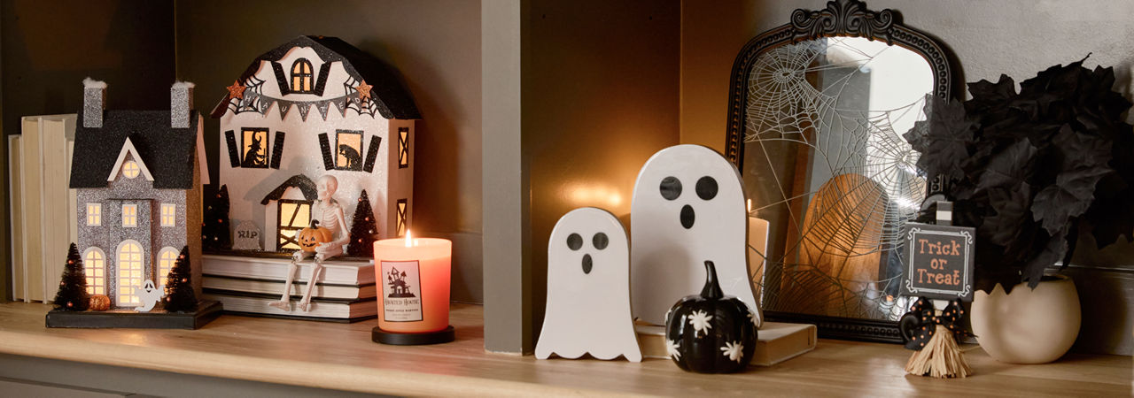 A neutral toned living room  decorated with classic Halloween decor from pOpshelf including ghosts, a spooky cozy blanket, plush pumpkin pillows, viral haunted houses with lights, moody Halloween framed wall art, and seasonal fall candles.